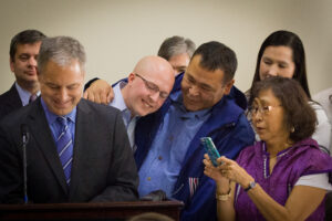 Representative Jonathan Kreiss-Tomkins of Sitka, Nome’s Bernadette Yaayuk Alvanna-Stimpfle, and others look on as Gov. Sean Parnell signs the bill into law. Photo: Matthew F. Smith, KNOM.