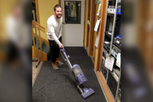 Davis Hovey uses a vacuum to clean the carpeting inside KNOM's radio studios.