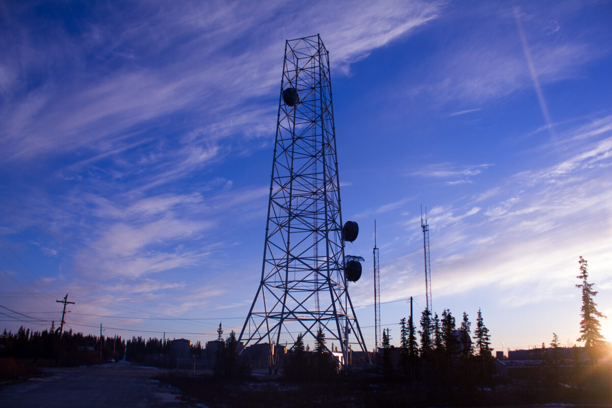 In Noorvik, the GCI tower juts up into the morning air. It is silhouetted against blue skies and partial clouds.