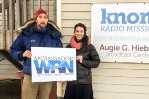 Ed and Margaret, holding an "Ambassador WRN" sign outside KNOM's studios.