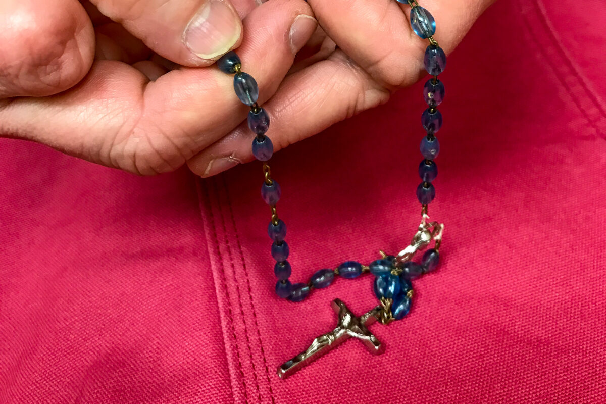 Hands holding Rosary beads over a pink cloth.