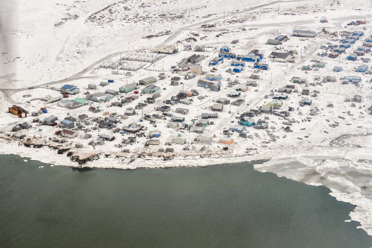 An aerial view over a snowy, coastal Alaska village in wintertime