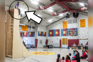 Nick Hanson, from the very top of a large, wooden structure, looks down on children sitting on the floor of the Kiana school gymnasium.