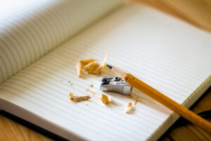 Pencil sharpener, pencil, and pencil shavings, on top of open, blank notebook