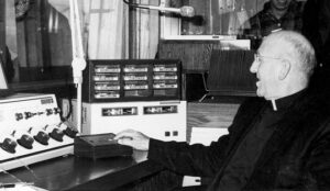 Black and white image of Catholic bishop pushing button on radio control console