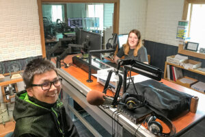Nome youth Jonathan Outwater sits behind a radio microphone in the studio with KNOM volunteer Karen Trop.