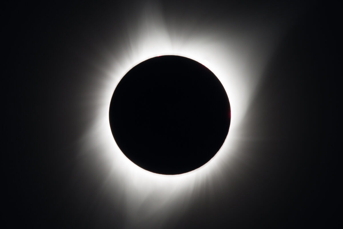 A total solar eclipse: a black sky with the sun completely blocked by the moon in silhouette, leaving only the white corona of the sun visible.