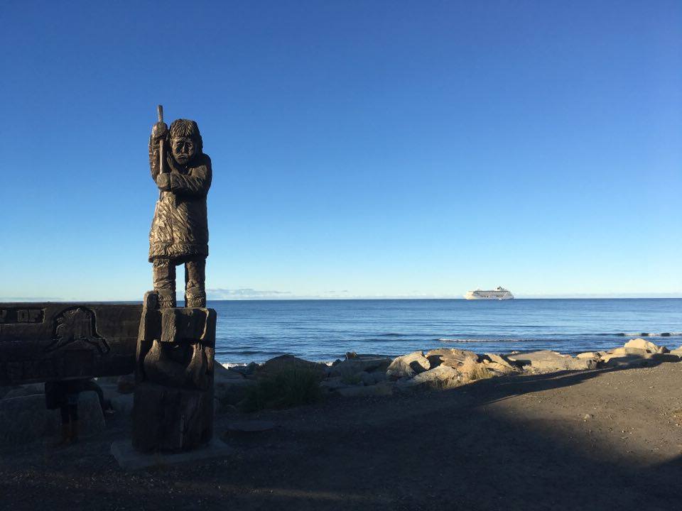 The cruise liner Crystal Serenity anchored offshore at Nome, with a Native statue in the foreground.