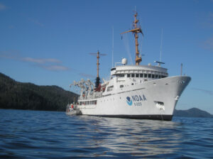 The NOAA Ship Fairweather with a forested coastline in the background.