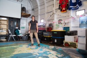 Crew member Geneviève Côté stands on the floor map of the Canadian Arctic in the converted helicopter hangar (Photo courtesy of Lia Nydes, 2017)