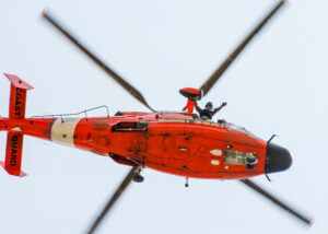 Orange and white Coast Guard helicopter flying directly overhead