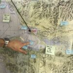 A Coast Guard pilot points to a large map covered with sticky notes marking the location of wildlife. The Coast Guard receives regular updates from government scientists to avoid disturbing game during training exercises.