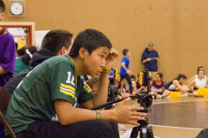 Student Broadcaster Mason Ivanoff lines up his shot at the Wrestling and Cheer Tournament in Unalakleet, AK.