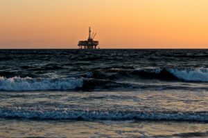 Offshore oil rig, viewed in the distance from the shore with waves crashing in the foreground