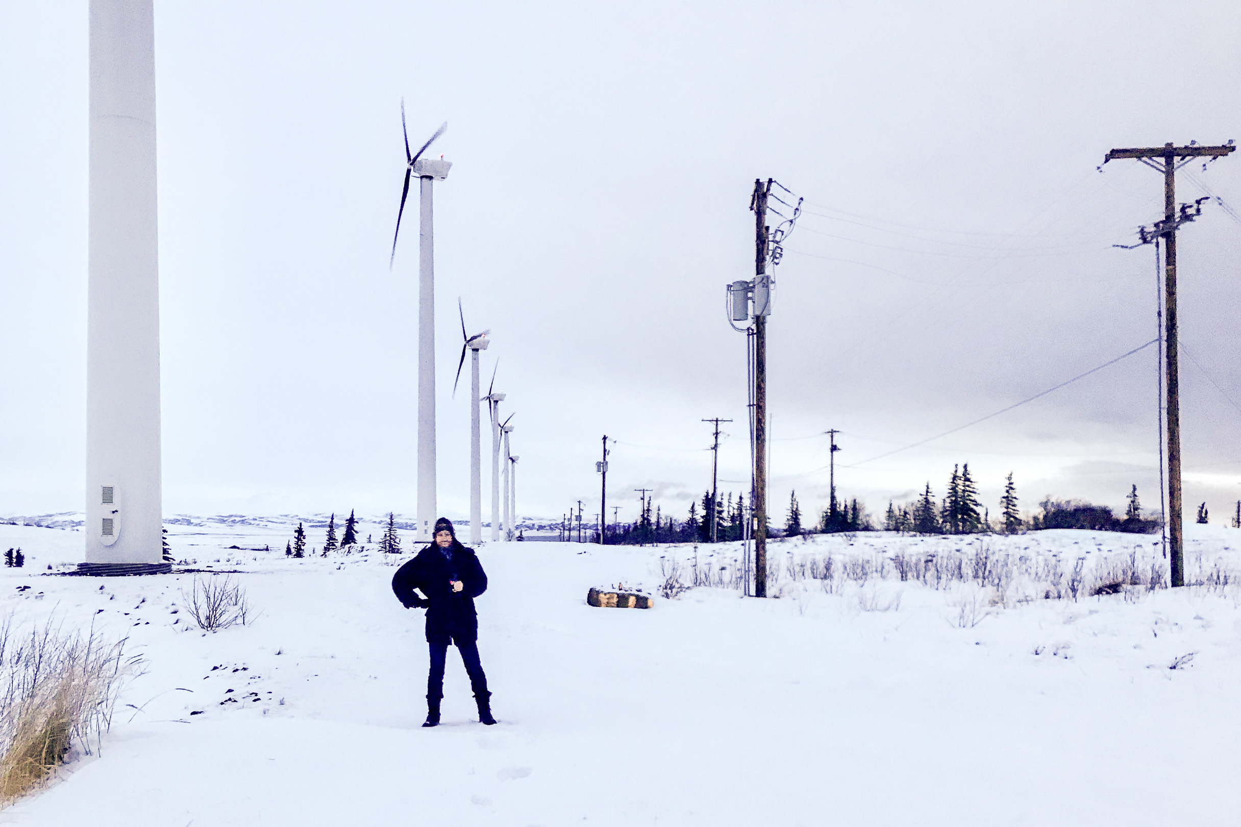 Man in heavy jacket stands in front of large array of wind turbines