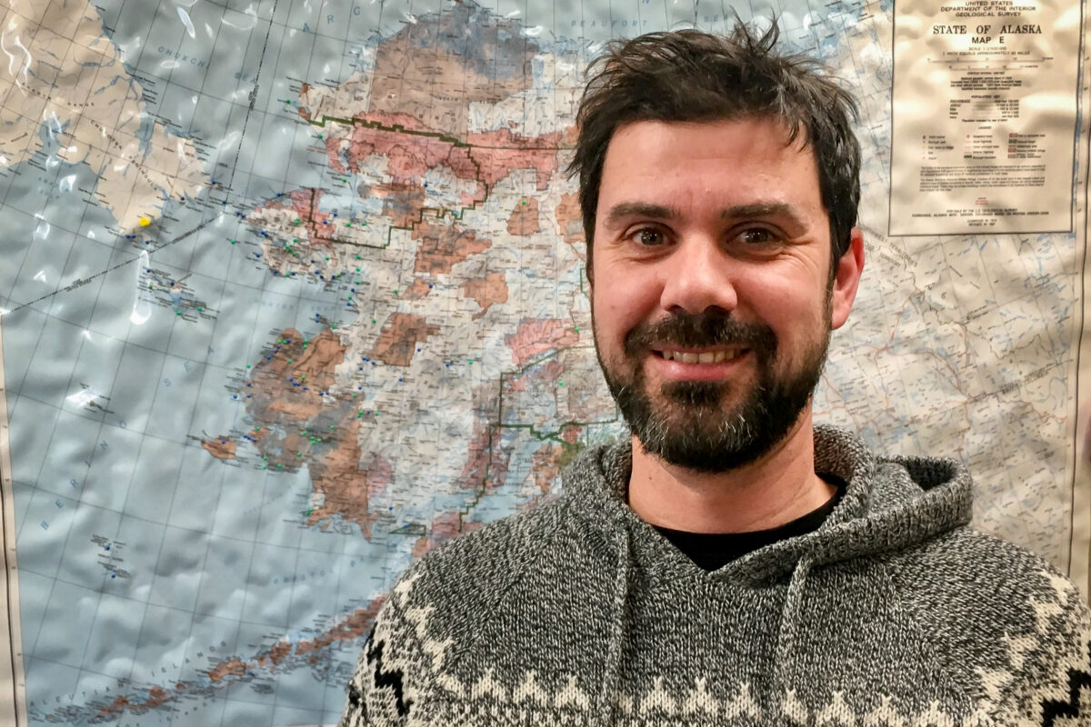 Bearded man stands in front of large map of Alaska