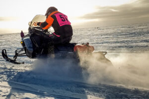 Racer on snowmachine (snowmobile), racing along the snow-covered, frozen Bering Sea near the shoreline of Nome.