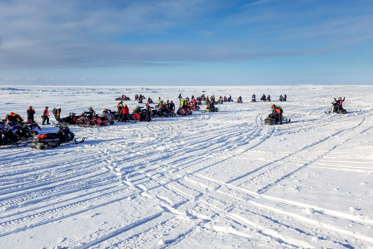 Racers on snowmobiles on snow-covered sea ice.