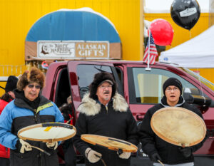 Three men sing on an Anchorage street holding Alaska-Native-style drums