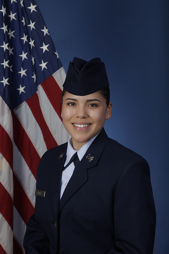 Woman in uniform poses in professional portrait, smiling in front of American flag.
