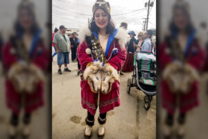 Woman stands in Nome street, smiling, wearing traditional Alaska Native clothing handed down through her family.