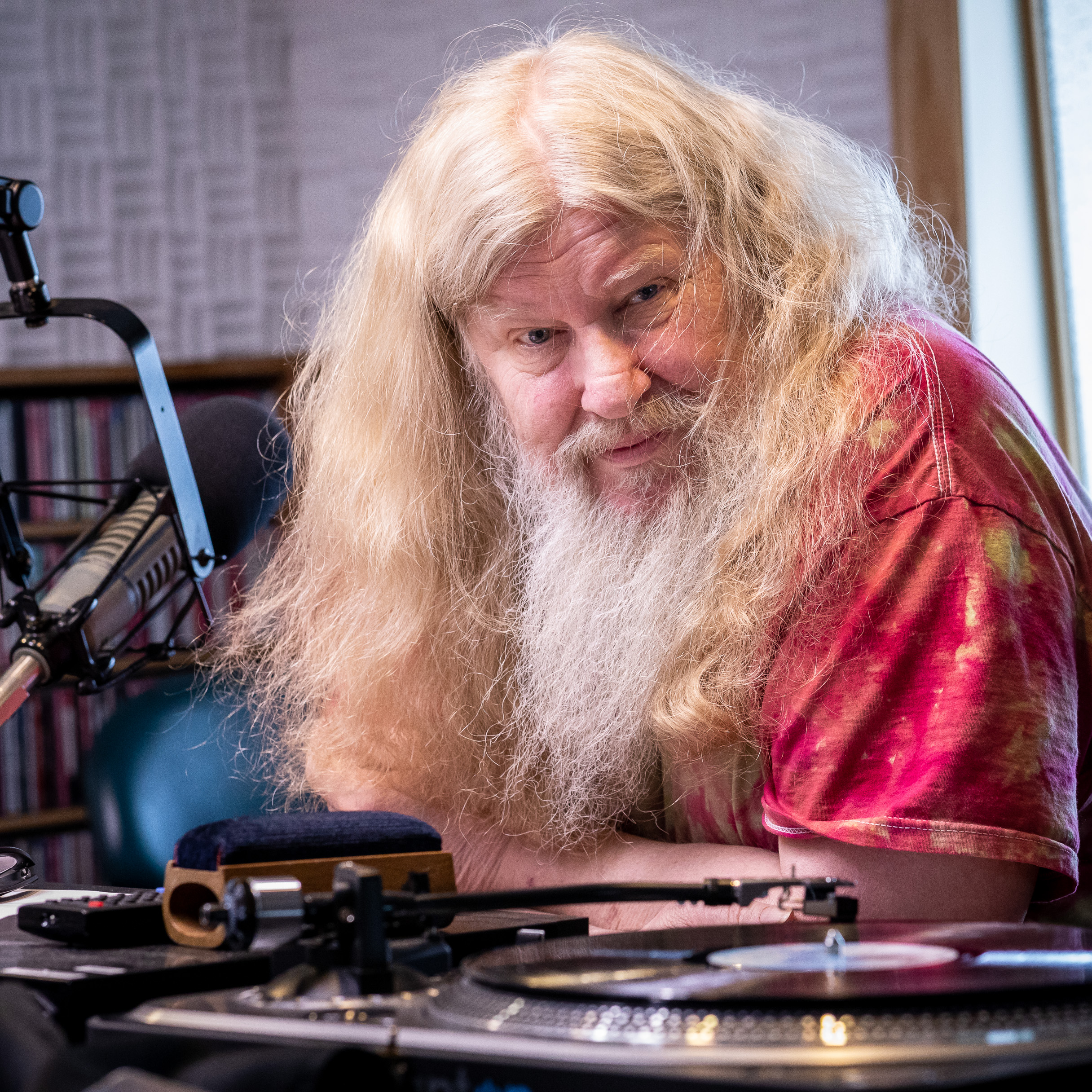 Dave Coler looks at the camera from behind a radio microphone and turntable.