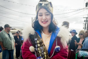 Lisa Lynch, wearing a deep red parka and other regalia, stands on a busy Front Street in Nome.