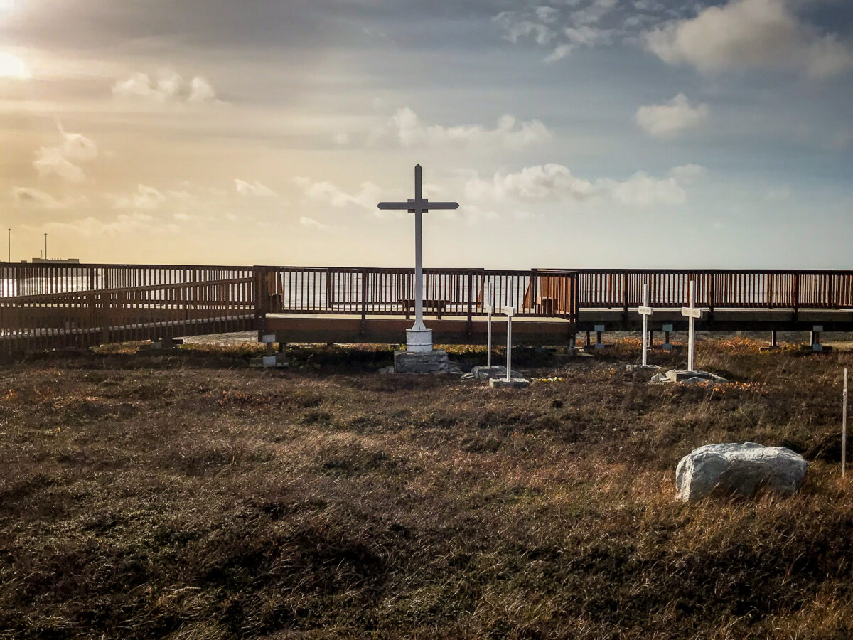 Landscape of cemetery with afternoon sky and Bering Sea in background.