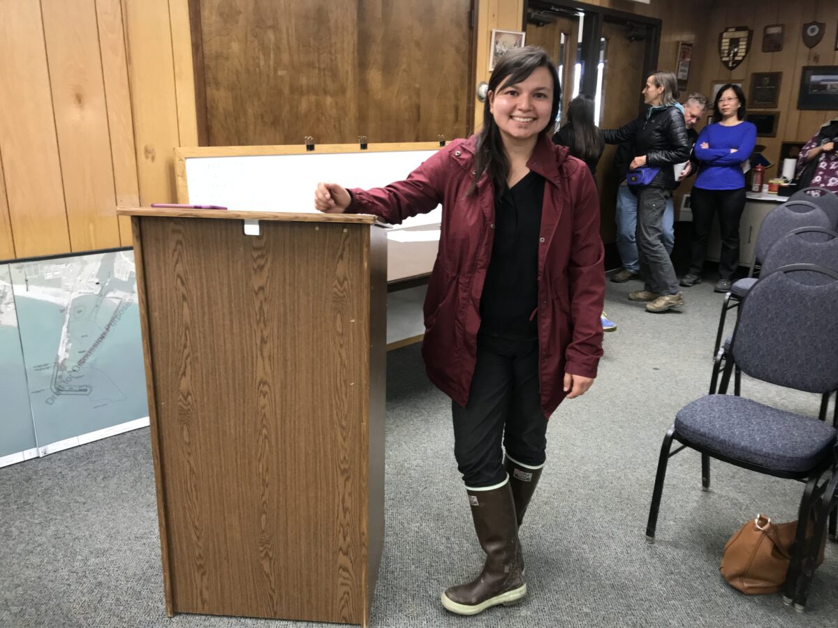 Woman stands at podium inside Nome City Council chambers.