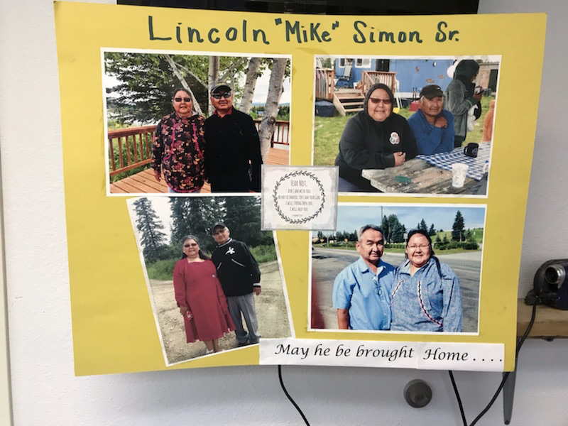 A yellow, homemade poster with photos of Lincoln "Mike" Simon with friends and loved ones. At the bottom, it reads: "May he be brought home."
