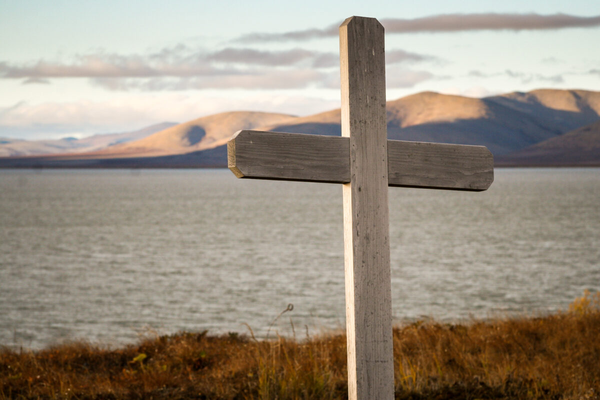 Wooden cross in foreground, large body of water and sub-Arctic mountain range in background