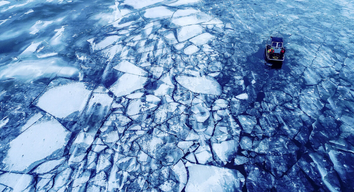 Aerial image of dark blue water, a field of ice chunks, and a small vessel involved in search-and-rescue efforts.