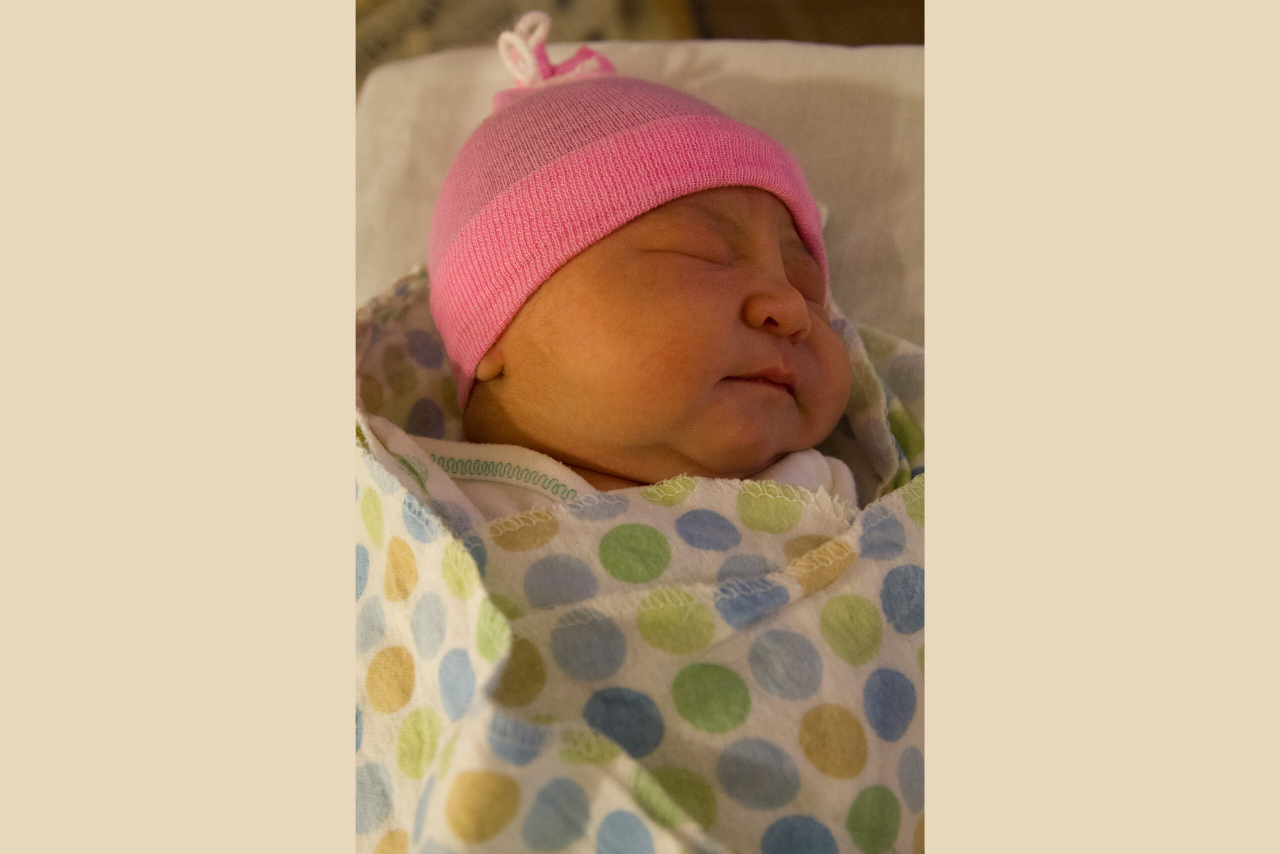 Image of newborn child in pink hat and polka-dotted blanket