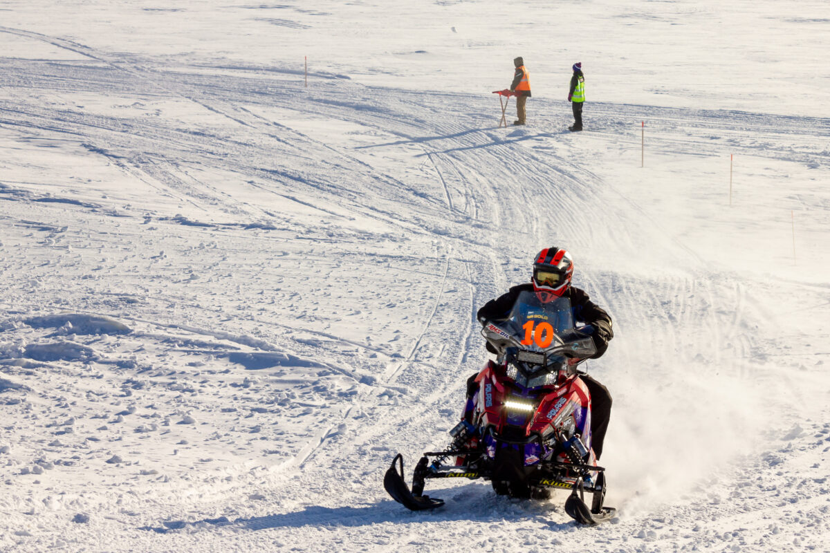 Snowmachine racer speeds up snow ramp, racing off of Bering Sea ice.
