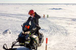 Snowmachine racer speeds up snow ramp, racing off of Bering Sea ice.
