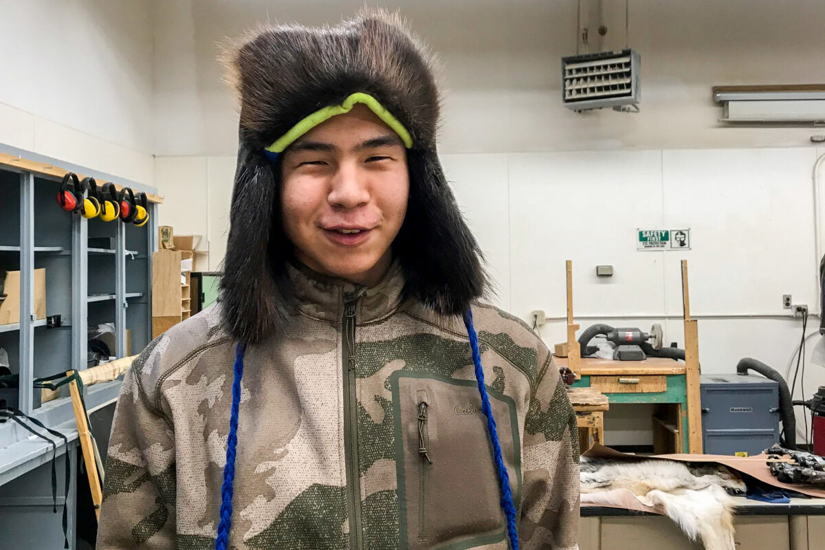Teenager stands inside high school workshop, wearing winter hat