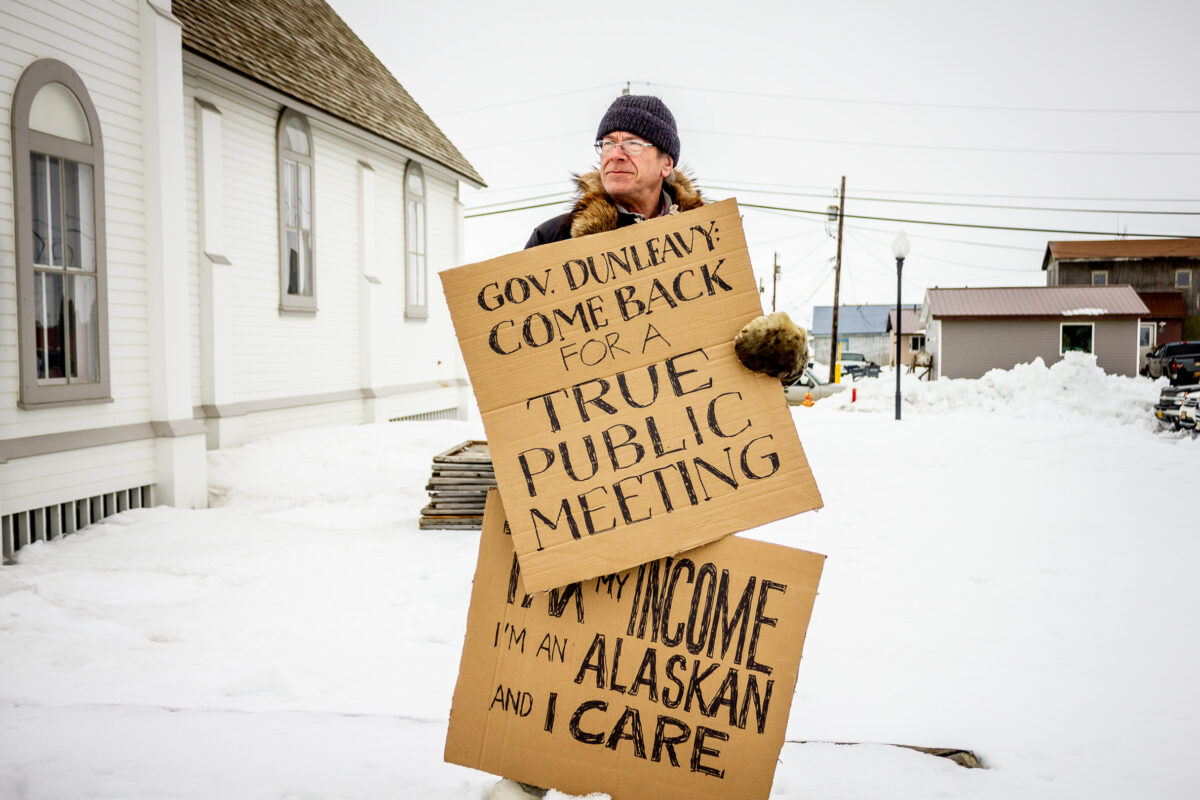 Man holding cardboard protest signs outside Nome community hall