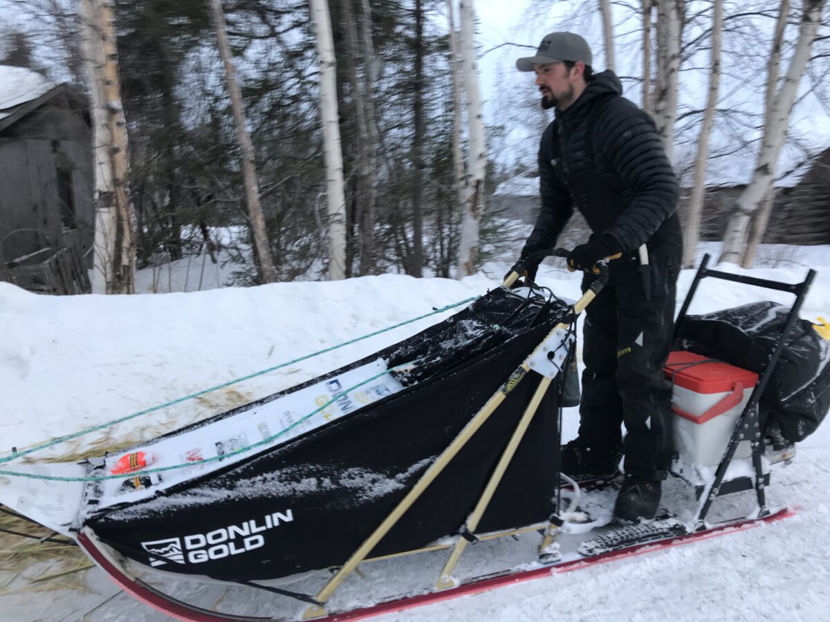Man in black parka rides sled along a snowy trail