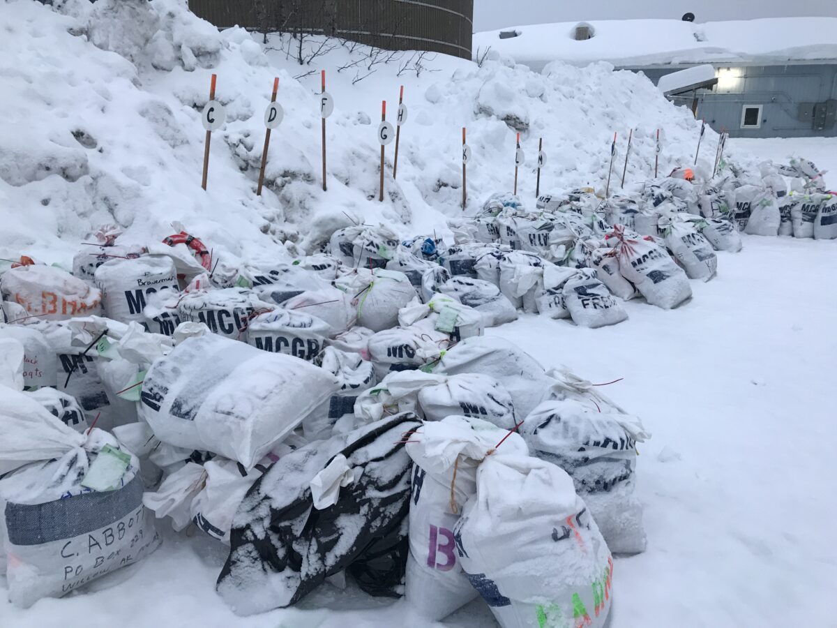 Snow-covered nylon bags, clustered together on the ground.