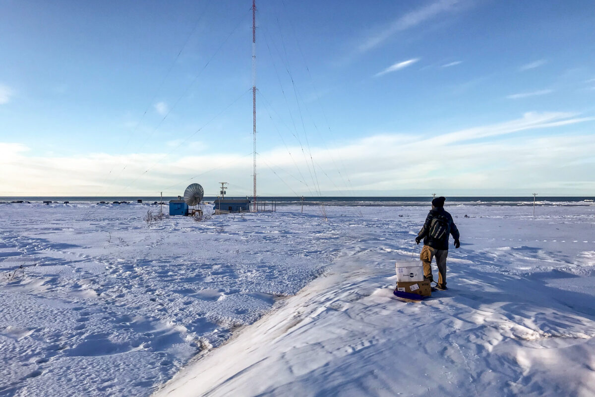 Man on snowshoes walks over snow drifts to remote AM transmitter tower site