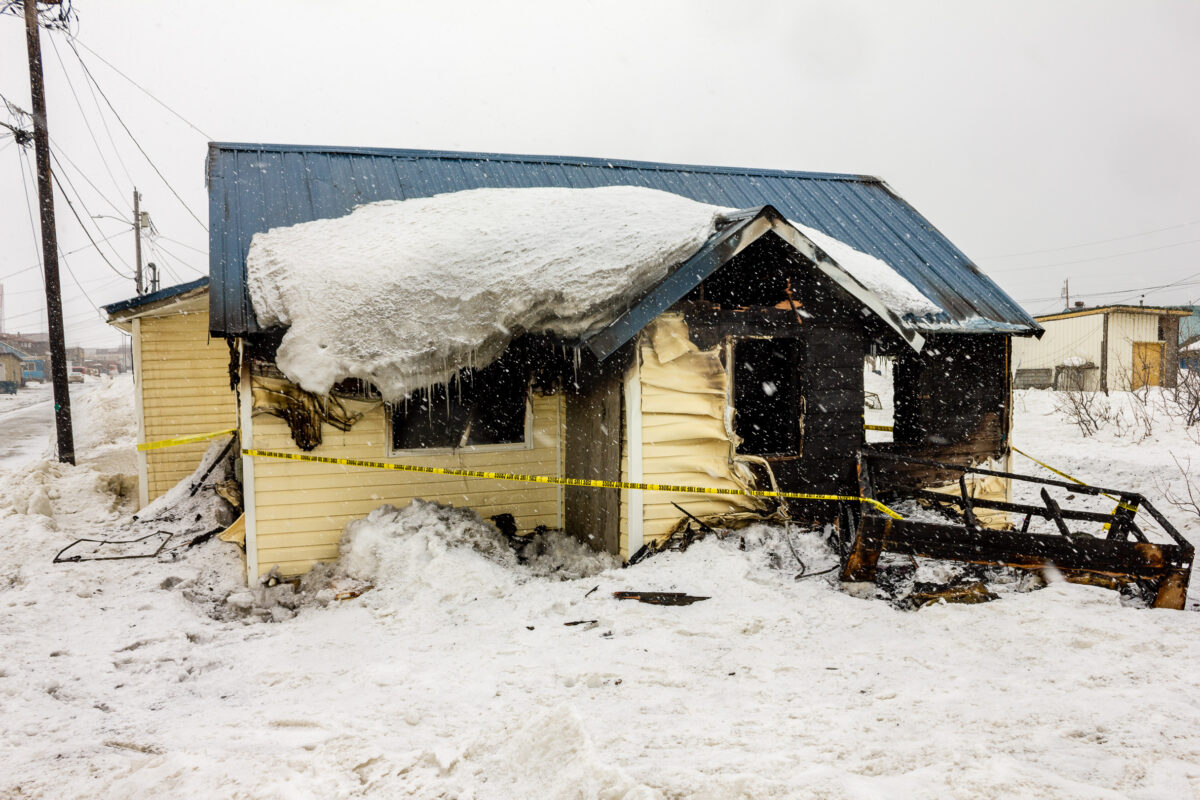 A house heavily damaged by fire, seen on a snowy afternoon in a rural Alaska town.