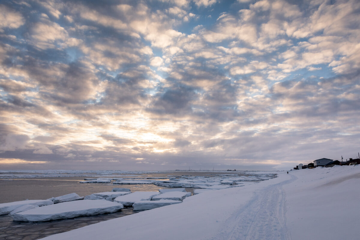 Sunset over a snowy shoreline with small icebergs dotting the ocean, stretching to the horizon