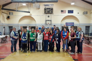 Group of people wearing colorful, reflective vests stand together inside a large gymnasium.