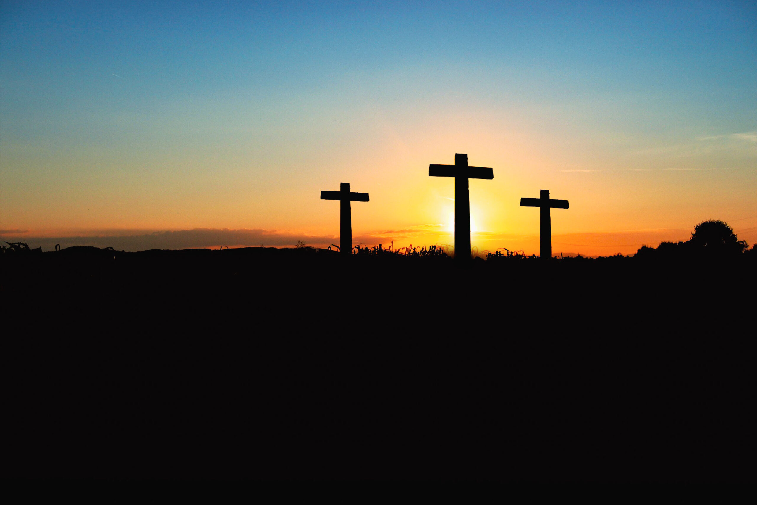 Silhouette of three crosses on a hillside set against a setting sun.