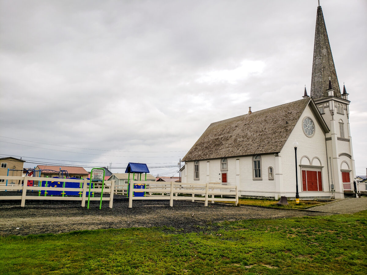 A children's playground area next to a grassy field and a white clapboard church