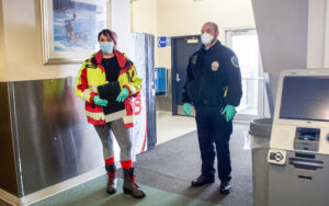 A female EMT and a male police officer wear masks and gloves in the terminal of the Nome airport.