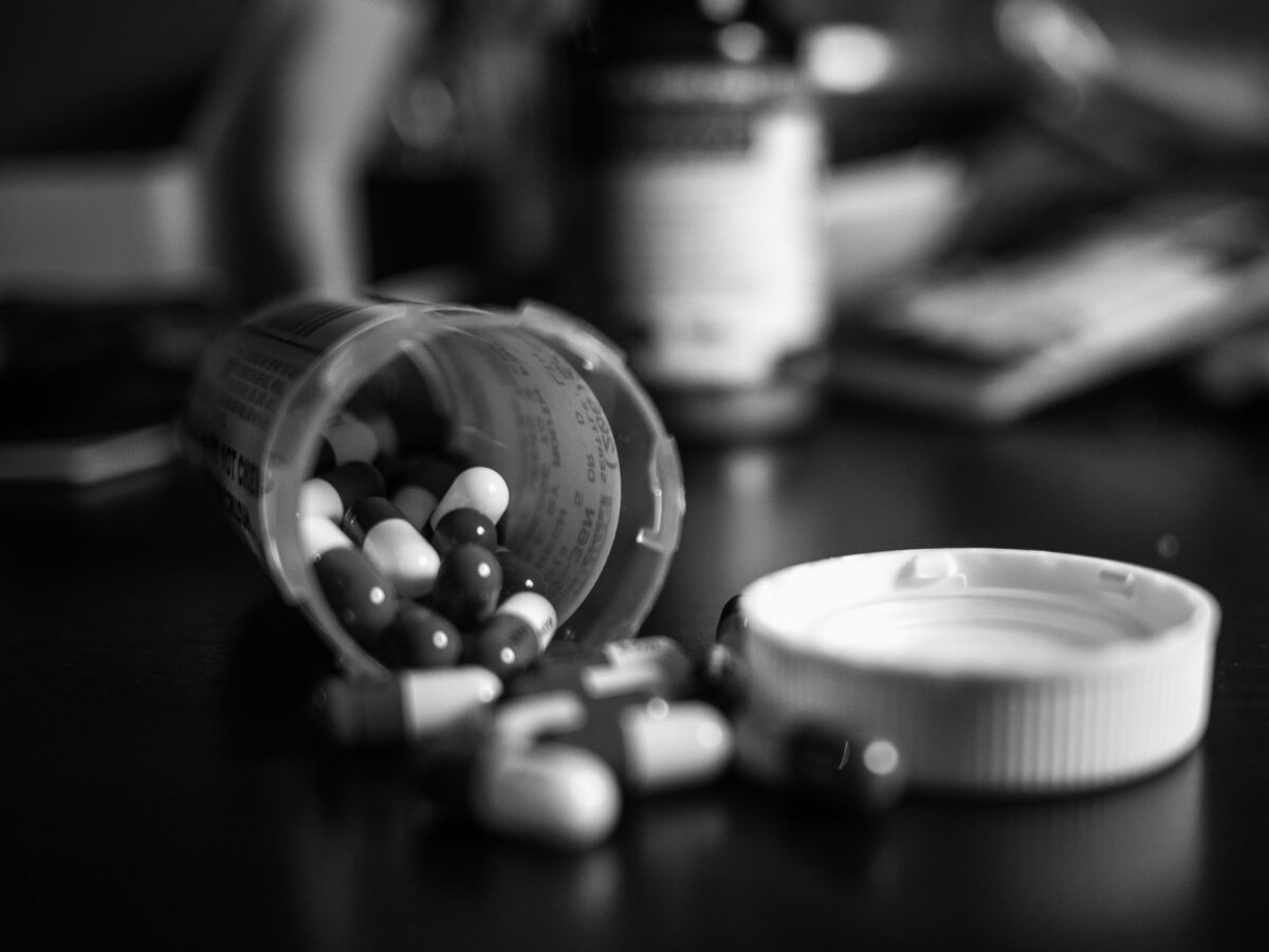 Black and white photo of prescription drugs falling out of bottle
