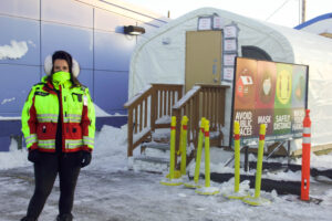 Woman wearing a bright reflective jacket and face covering standing outside COVID tent