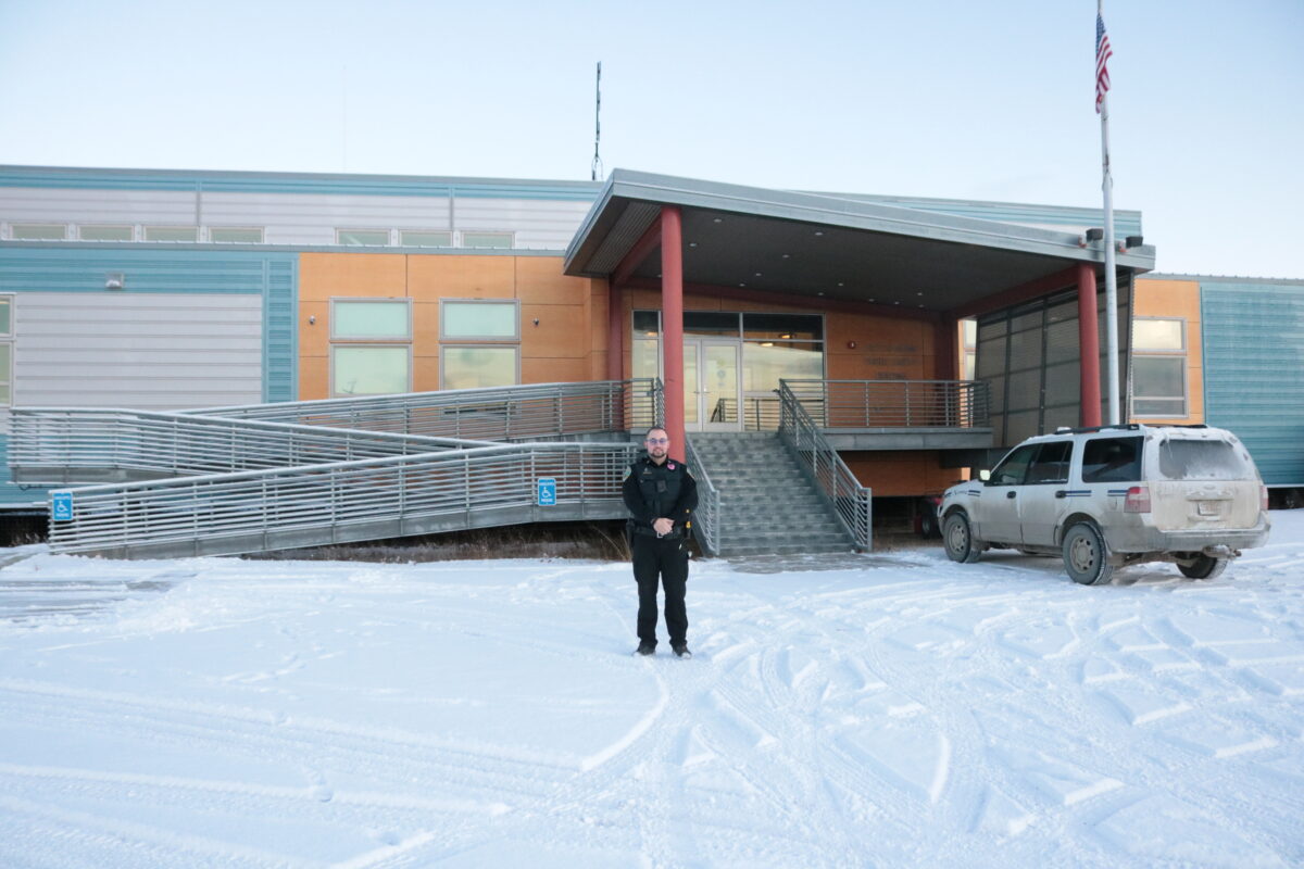 Police officer standing in front of Nome Police Dept. in the winter.