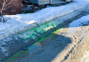 A photo of a snow bank with green liquid on it seeping into the street below in Nome, Alaska.